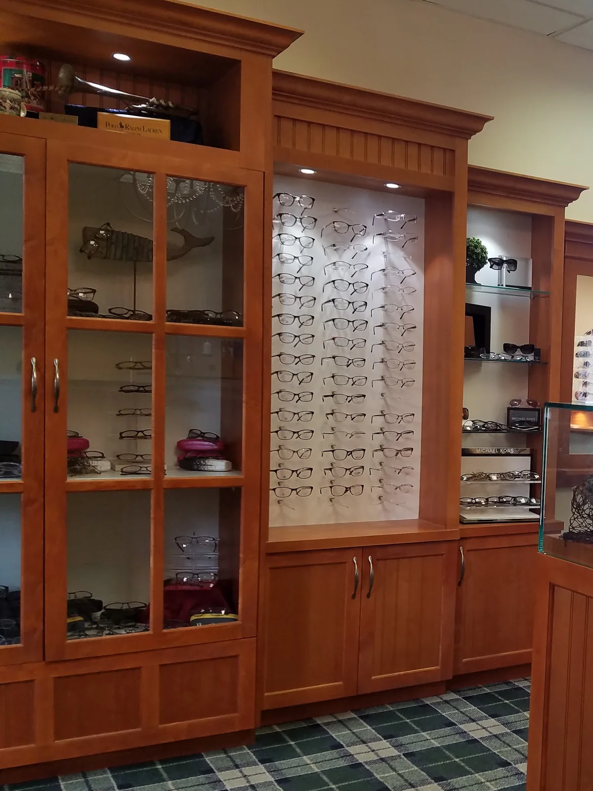The optical at Evergreen Eye Care: cherry display cabinetry and a lit wall of eyeglass frames.