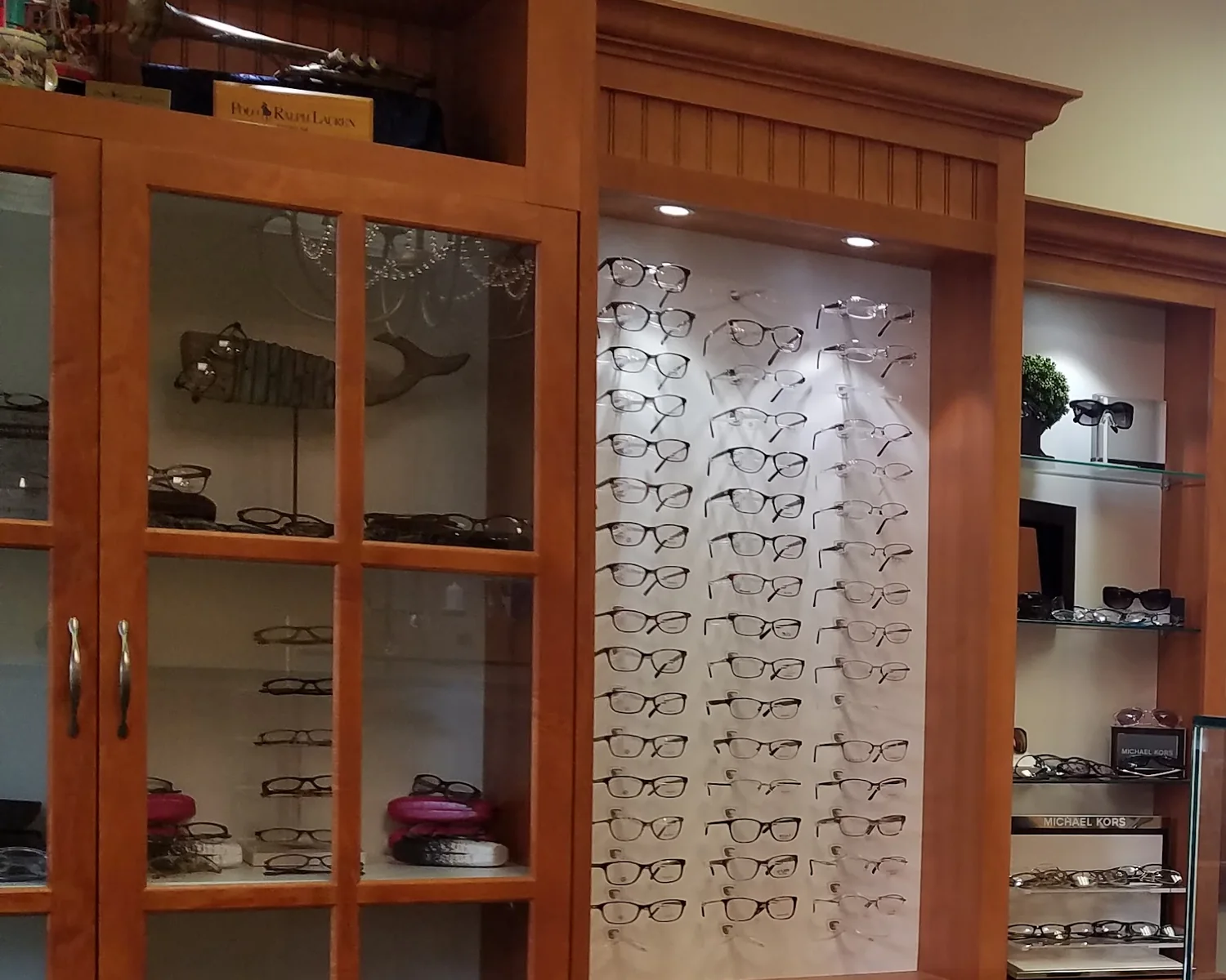 The optical at Evergreen Eye Care: cherry display cabinetry and a lit wall of eyeglass frames.